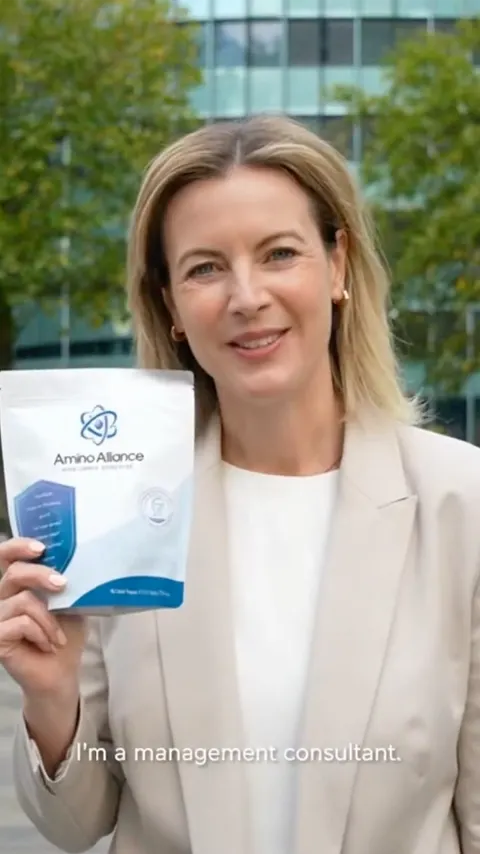 A woman in a pale blazer holding an Amino Alliance pouch to camera outside an office building, with a caption reading I am a management consultant.