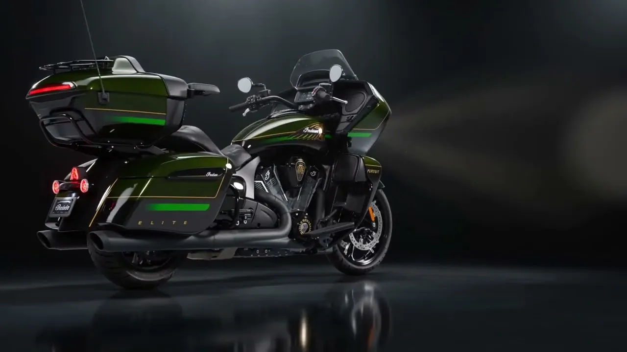 The green and black Indian Elite on a dark reflective studio floor, three-quarter rear view, gold pinstriping and the ELITE lettering on the pannier catching a single overhead light.