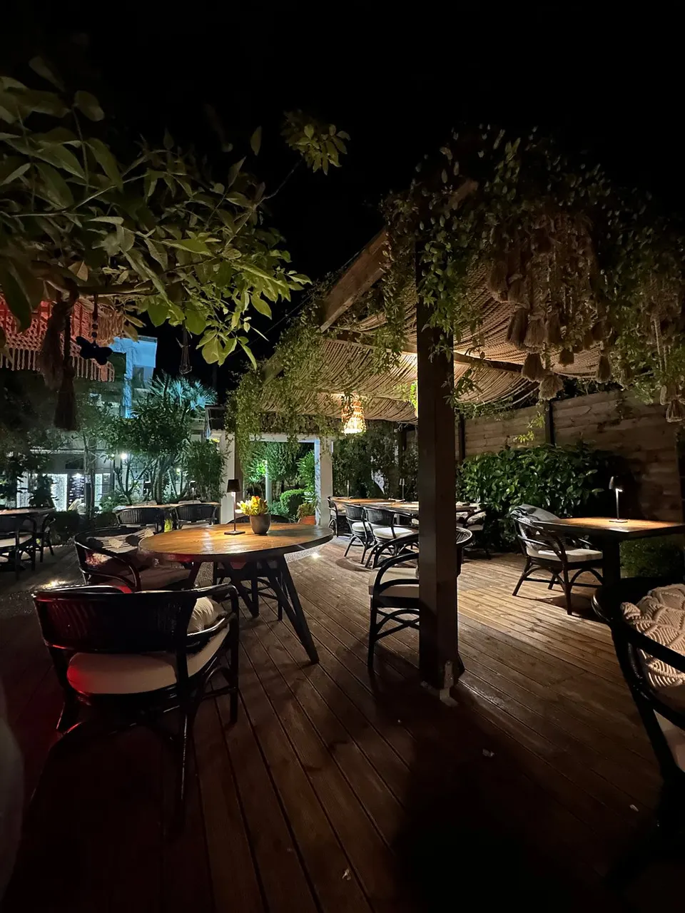 The terrace at Mariposa after dark, wooden decking, cane shades, planting overhead and a lit table in the middle distance.