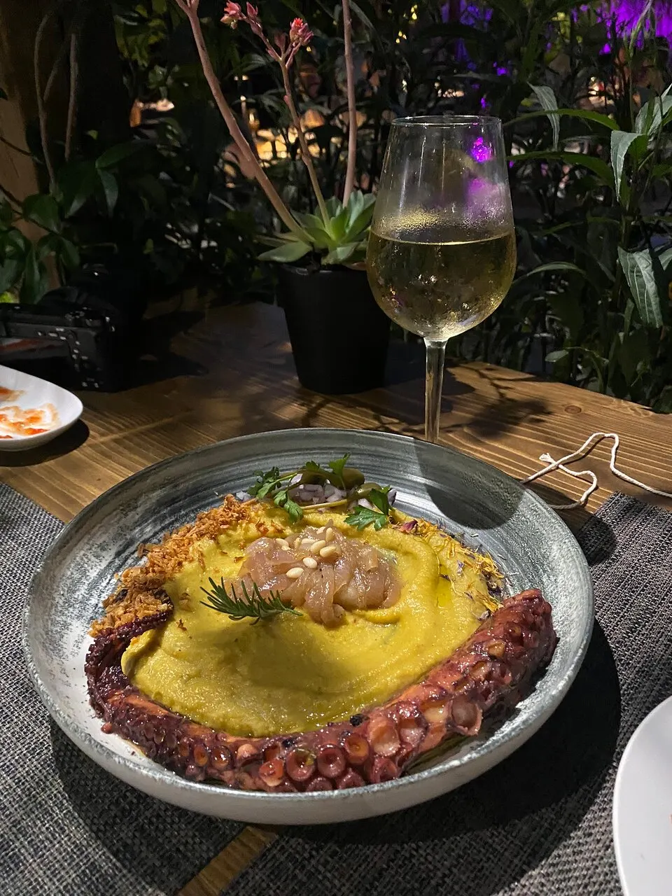 Grilled octopus curled over yellow fava purée in a stone bowl, topped with pickled onion and dill, shot at the table at night.